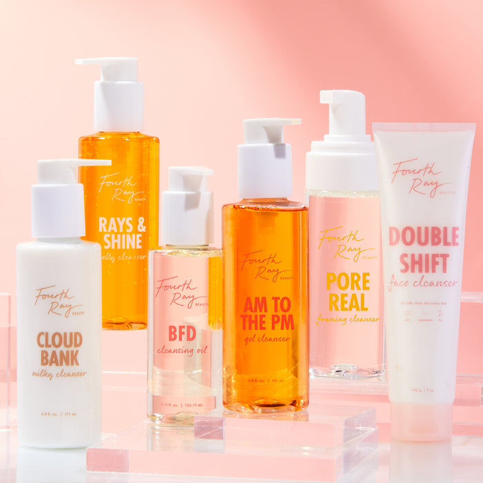 AM to the PM Gel Cleanser by ColourPop Fourth Ray Beauty stands centered, an amber gel pump bottle showcased on clear acrylic risers, surrounded by other Fourth Ray face cleansers against a pink gradient background.