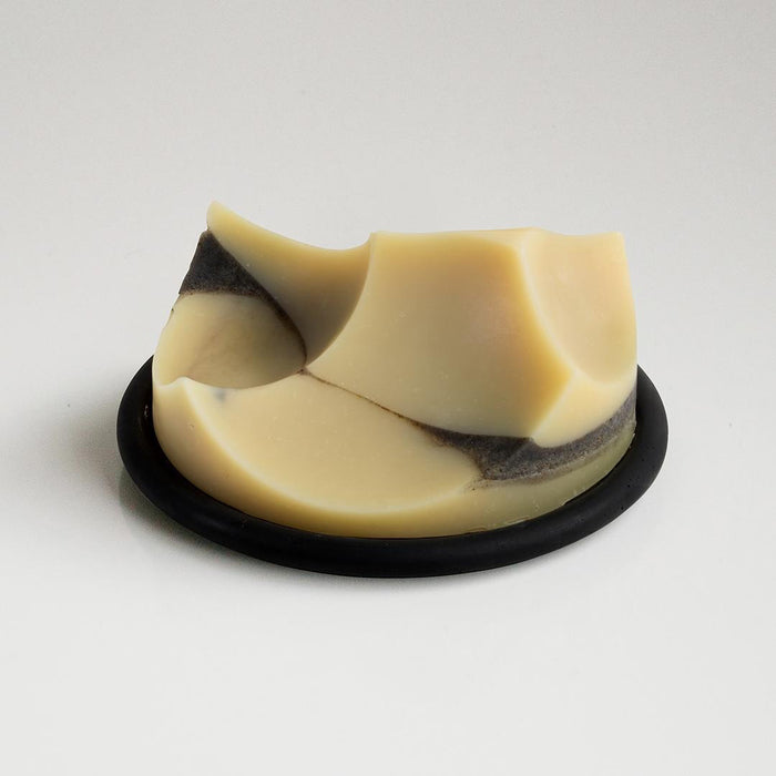 The UME Studio Black Bouton Erode Soap Dish, large and round with three holes, rests on a handmade light gray textured coaster, casting a soft shadow to the right.
