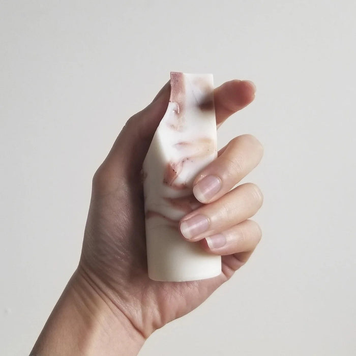The UME - LAVENDER CREME MINI ERODE SOAP by UME STUDIO is a cylindrical bar with marbled white and brown swirls, standing upright on a white surface. Its top edge is slightly curved and uneven.