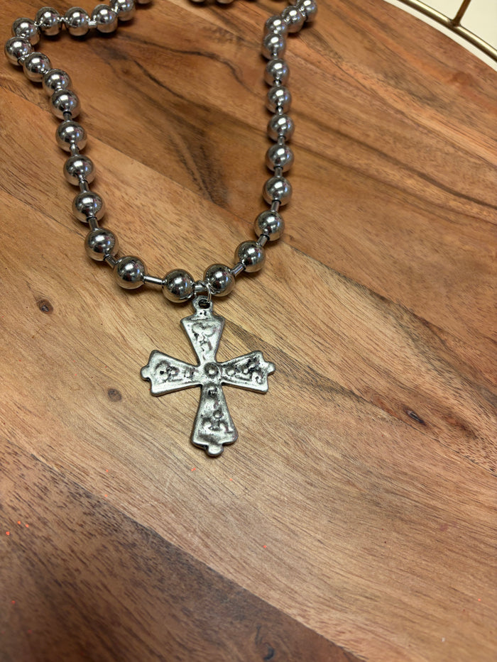 Lula 'n' Lee ball chain cross necklace hanging on a display, showcasing its sleek metal design and simple religious pendant.