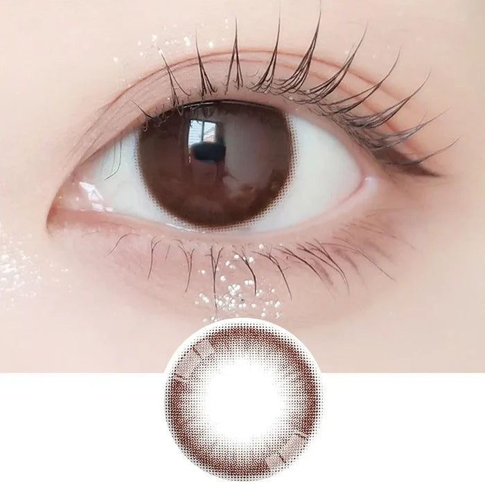 Close-up shot of model's eye adorned with Ann365 JUST Choco daily color contact lenses with prescription, paired with clean-girl eye makeup, showing the brightening and enlarging effect of the circle contact lens on dark brown eyes, above a cutout of the contact lens with limbal ring on a white background.