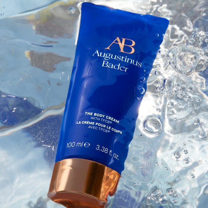 Augustinus Bader The Body Cream tube in blue with gold cap on water
