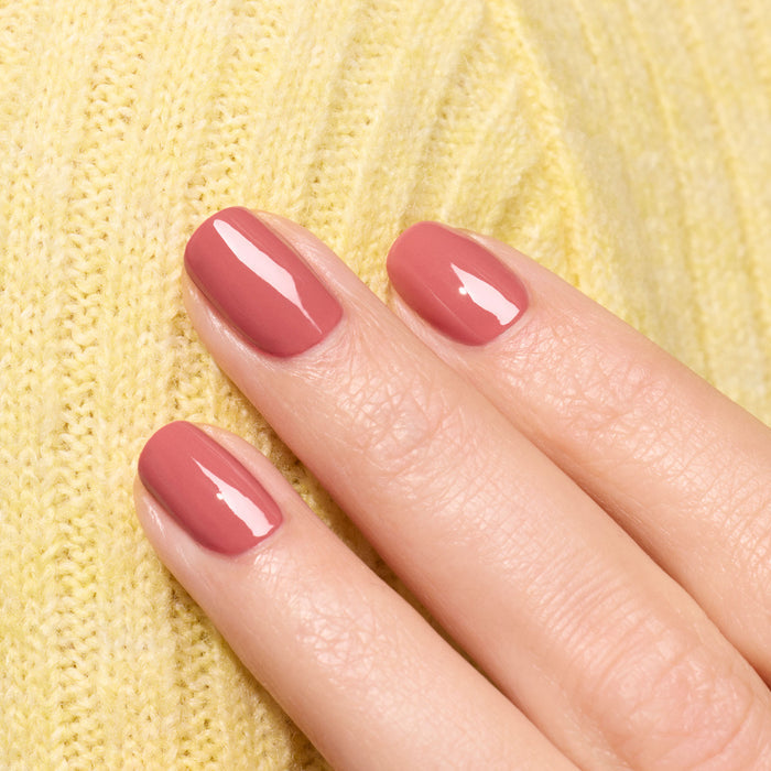 A close-up of a hand with neatly manicured nails painted in Manucurist’s Bois de Rose shade, resting on textured yellow knit fabric.