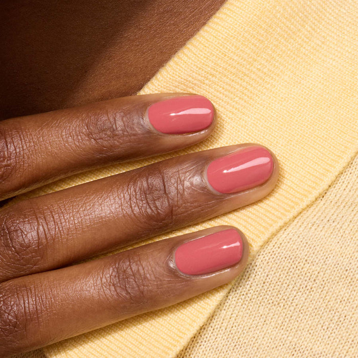 A hand with neatly manicured nails painted in Manucurist's Bois de Rose from the Green™ range rests on light yellow textured fabric.