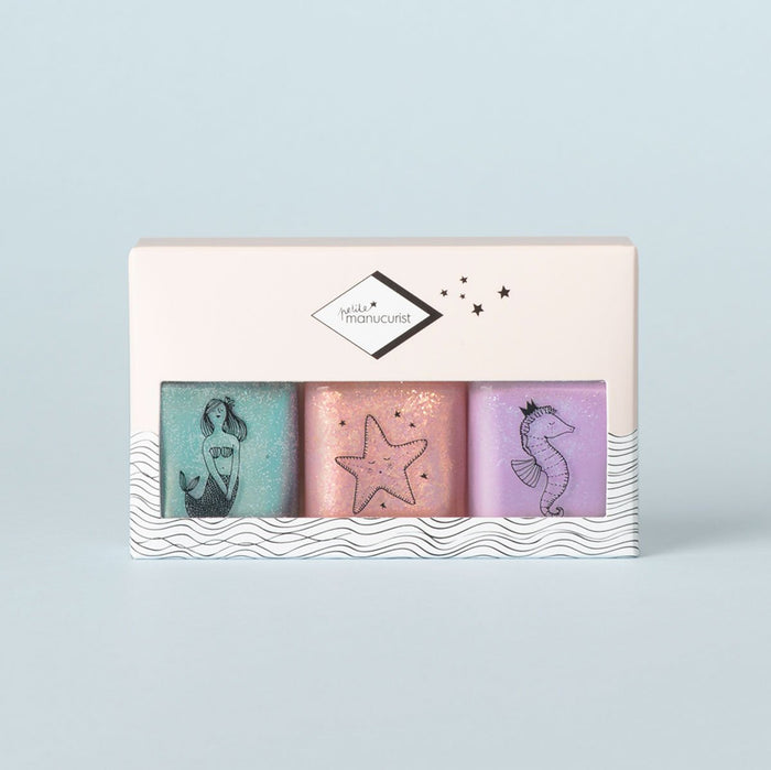 The Manucurist Bonnie Stella Janis Trio is a pastel kids nail polish set with three non-toxic shades—turquoise, pink, and purple—each with a sea-themed illustration, all packaged in a white box decorated with waves and stars.