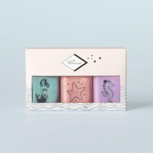 The Manucurist Bonnie Stella Janis Trio is a pastel kids nail polish set with three non-toxic shades—turquoise, pink, and purple—each with a sea-themed illustration, all packaged in a white box decorated with waves and stars.