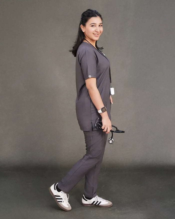 female doctor wearing gray Medical scrubs Pakistan with a stethoscope, standing against a gray background.