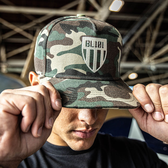 Camouflage snapback hat with white embroidered BL101 shield logo design on the front