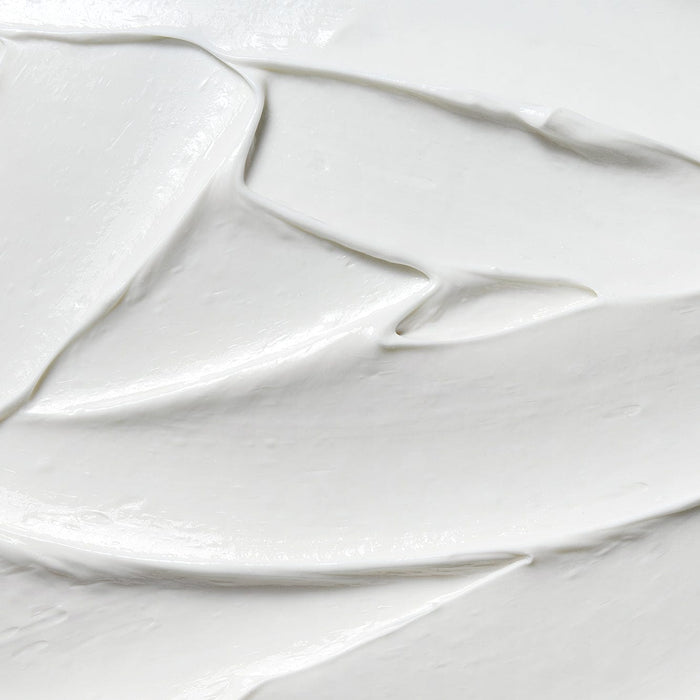 Close-up texture of smooth white cream with soft peaks and a glossy finish, showing the rich, nourishing consistency of a foot care formula.