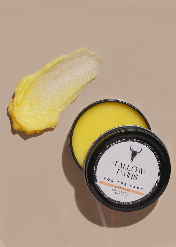 An open tin of For the Face tallow balm beside a swipe of bright yellow balm.