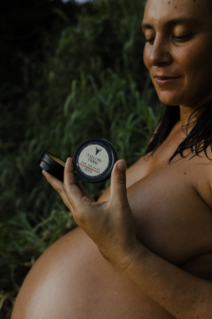 A pregnant woman outdoors holding a small tin of Tallow Twins balm.