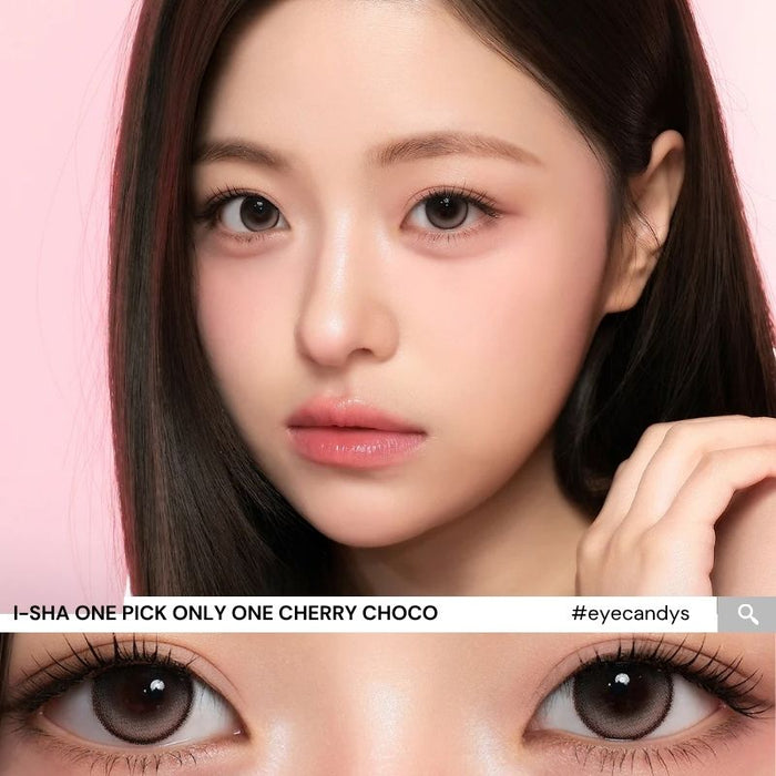 A woman with flawless skin and long dark hair poses against a pink background. The image also features a close-up of her brown eyes wearing i-Sha One Pick Only One 1-Day Cherry Choco colored contacts from i-Sha, which create a natural dolly eye effect with their rich chocolate brown shade.