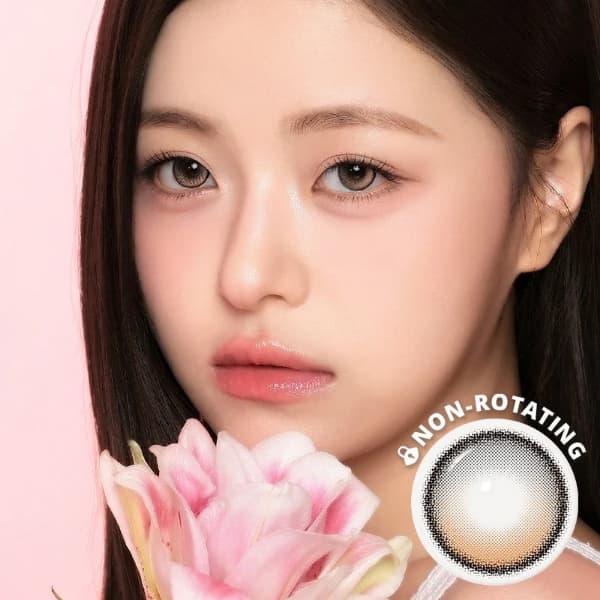 A young woman with long dark hair holds a pink lily flower near her face. She has soft makeup and is wearing i-Sha One Pick Only One 1-Day Cherry Choco contact lenses by i-Sha for a natural dolly eye effect. A circular "NON-ROTATING" label appears in the lower right corner of the image.