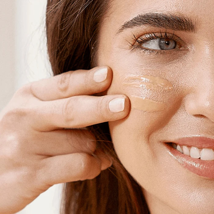 Woman applying tinted mineral sunscreen to cheek, ISDIN Eryfotona Ageless SPF 50