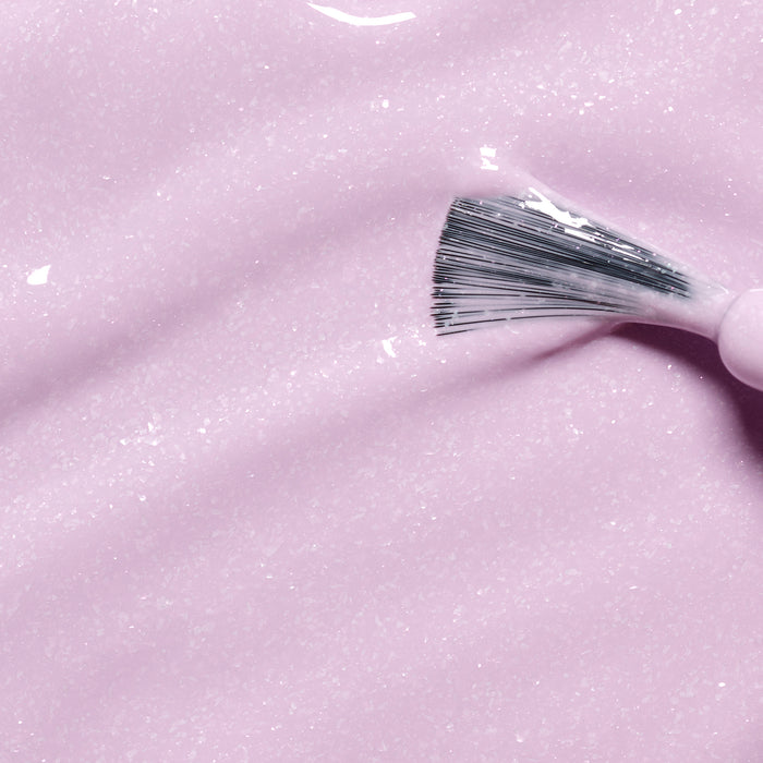 A close-up of a brush spreading Janis the Seahorse, a creamy, light pink kids' nail polish by Manucurist with a glossy texture and enriched with naturally sourced ingredients.