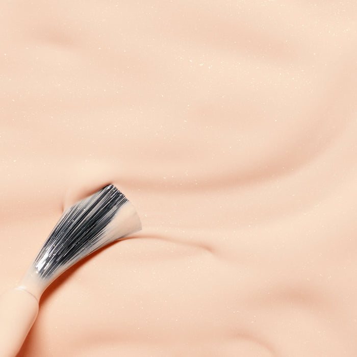 Joy the Bear Cub by Manucurist sits on a smooth, peach-colored surface with a soft, creamy texture and subtle sparkles, reminiscent of peach glitter polish made from naturally sourced ingredients.