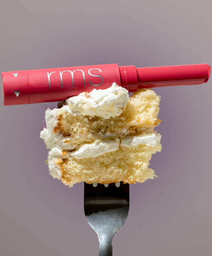 Legendary Serum Lipstick in a vibrant pink shade resting on a fork with a piece of vanilla cake topped with white frosting, showcasing clean beauty and natural ingredients.