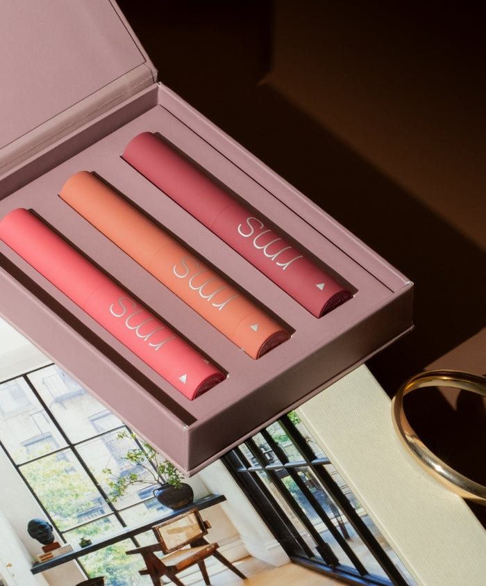 Legends To Love Kit featuring three sleek lip products in coral, peach, and rose shades displayed in an elegant pink box with natural light and a modern interior background.