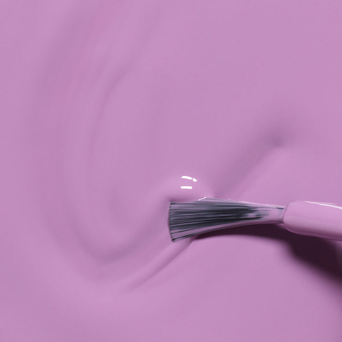 A close-up of the Manucurist Lily the Unicorn brush spreading smooth, glossy purple polish across a surface, creating gentle swirls and reflections.