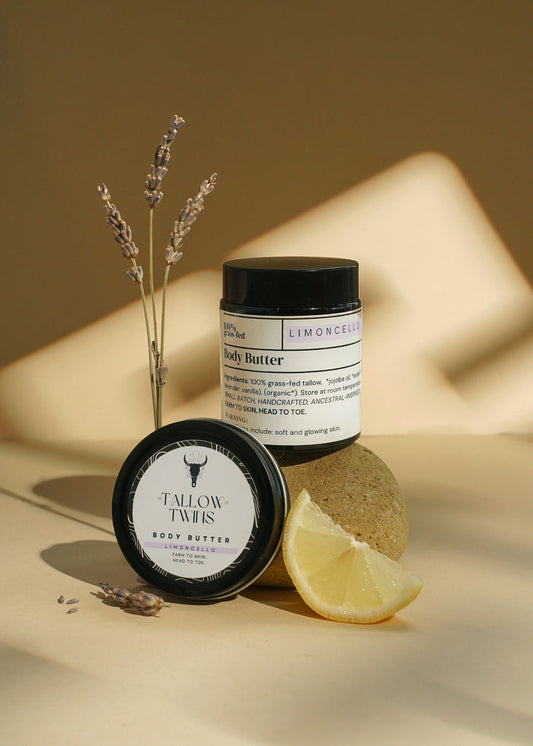 A jar of Limoncello Body Butter with its lid, lavender sprigs and a lemon wedge.