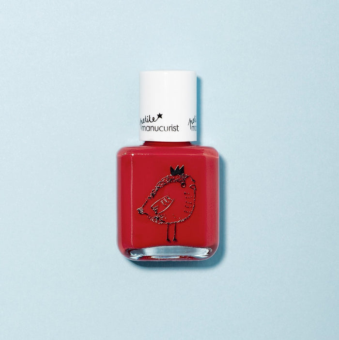 A bottle of Manucurist's kids' nail polish, "Lucette the Warbler," with a white cap and a cute crowned bird drawing on front. Made with naturally sourced ingredients, it pops against the light blue background.