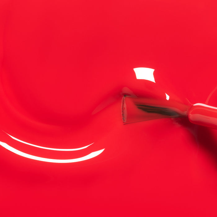A close-up of a Manucurist Lucette the Warbler nail polish brush spreading bright red kids' polish, with shiny reflections on the glossy surface—perfect for little hands and made from naturally sourced ingredients.