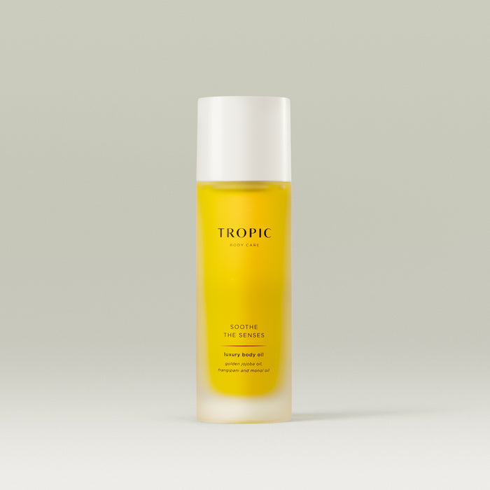 Tropic Soothe The Senses luxury body oil with golden jojoba oil, frangipani, and monoi oil in a sleek frosted bottle.
