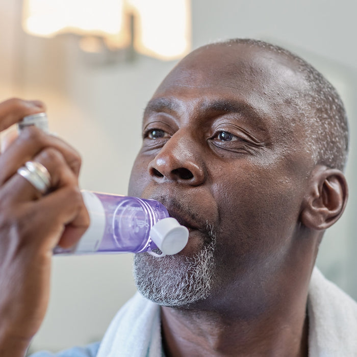 Man using a purple inhaler device with a blurred background