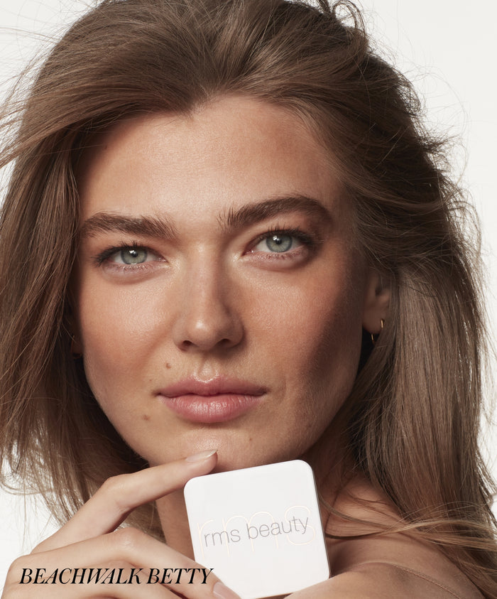 Close-up of a woman with natural makeup holding a white compact of ReDimension Hydra Bronzer by RMS Beauty, highlighting clean beauty and skincare-infused makeup.