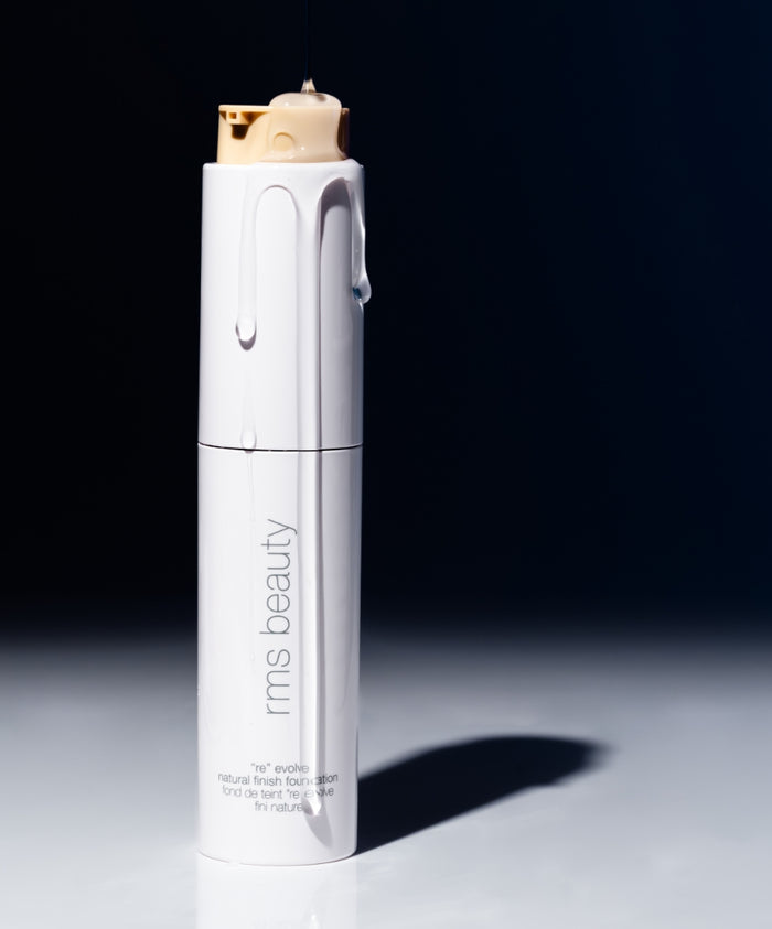 ReEvolve Natural Finish Liquid Foundation with smooth liquid texture dripping from the top of a sleek white rms beauty bottle, showcasing clean beauty and natural ingredients.