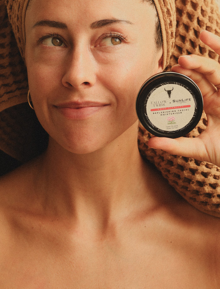 A woman with her hair wrapped in a towel holding the Tallow Twins x SunLife Rose Vitality facial moisturiser.