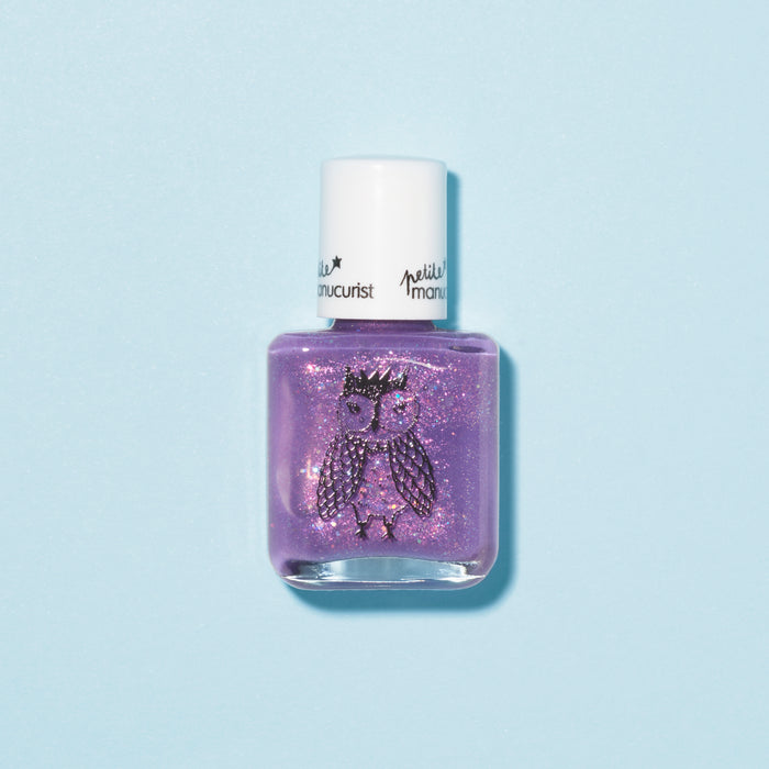 A bottle of Manucurist Scarlett the Owl kids' nail polish in purple glitter, featuring a white cap and a crowned owl illustration on the front, set against a light blue background.