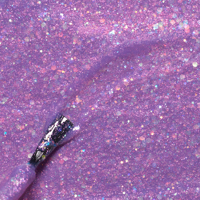 A close-up of a brush applying Manucurist’s Scarlett the Owl kids' nail polish—a sparkly purple glitter with multicolored flecks—on a matching glittery purple surface.