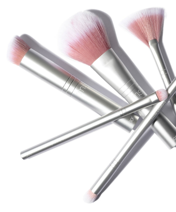 Close-up of several pink-tipped makeup brushes with silver handles, featuring the Skin2Skin Everything Eye Polish Brush among them in a clean beauty makeup setting.