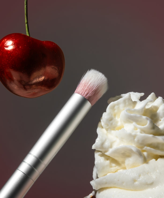 Skin2Skin Everything Eye Polish Brush with soft bristles near a cherry and whipped cream, highlighting precision and gentle application for clean beauty makeup looks.