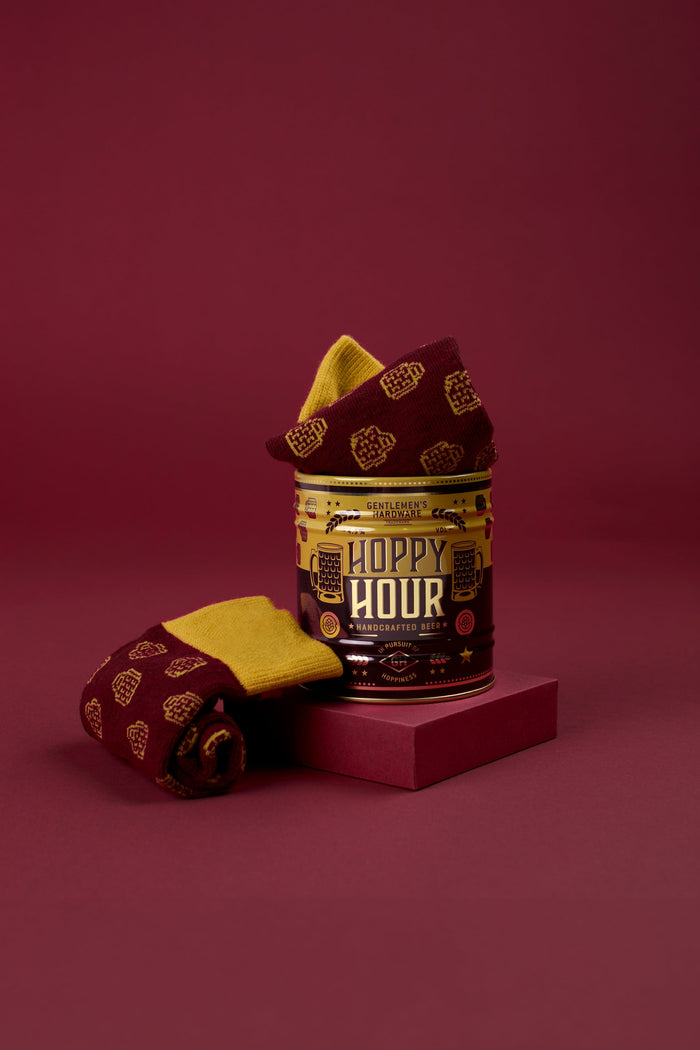 Folded beer-themed socks with gold pattern beside Hoppy Hour sock can