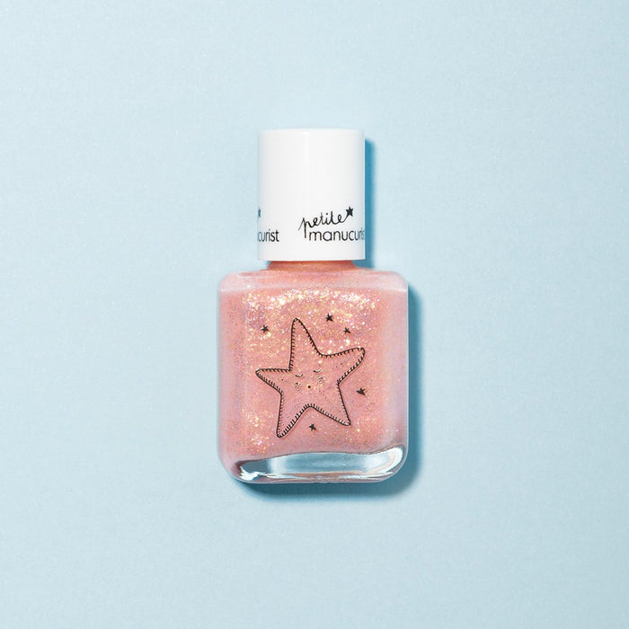 A bottle of Manucurist's Stella the Starfish pale pink kids nail polish with a white cap, featuring black outlined stars and small star designs on the front, is placed on a light blue background.