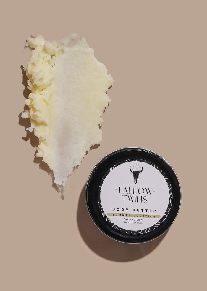 A tin of Summer Solstice Body Butter beside a thick swipe of pale yellow body butter.