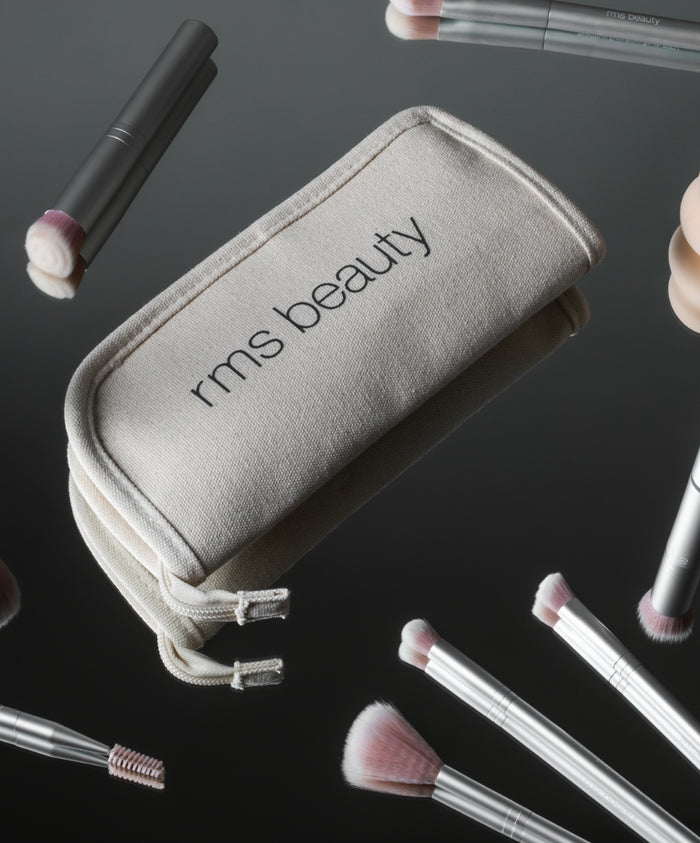 The Artist Toolkit featuring a beige fabric case with "rms beauty" printed on it, surrounded by various clean beauty makeup brushes with soft pink bristles and silver handles.