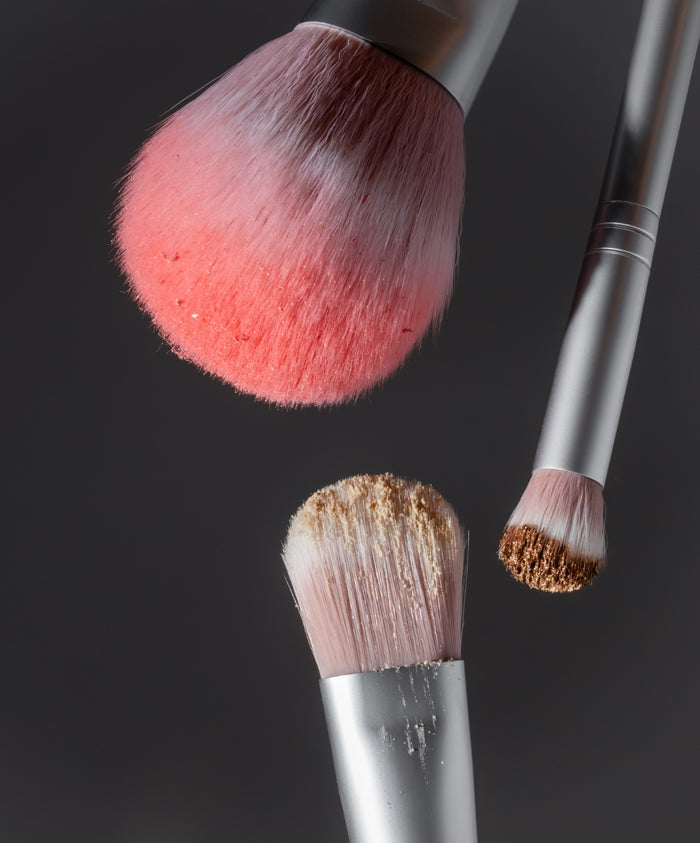 Close-up of three makeup brushes with pink bristles coated with powder and pigment, highlighting softness and detail of The Artist Toolkit.