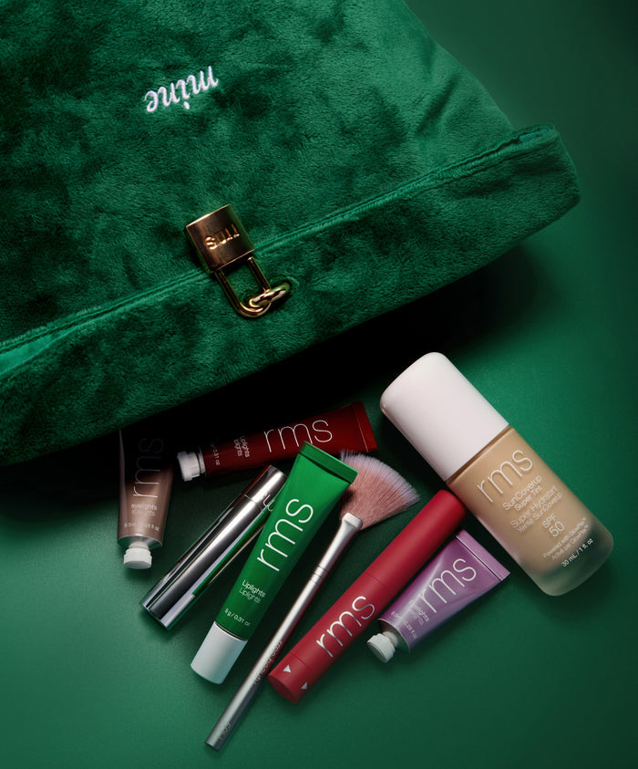 The Chameleon 2-Piece Set featuring a green velvet bag with gold clasp and an assortment of RMS Beauty clean, cruelty-free makeup and skincare products with natural ingredients.