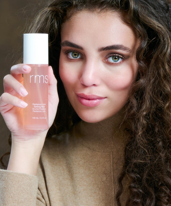 Woman with curly hair holding a radiant pink mist bottle near her face, showcasing The Prep & Set Duo for clean beauty and skincare infused makeup.