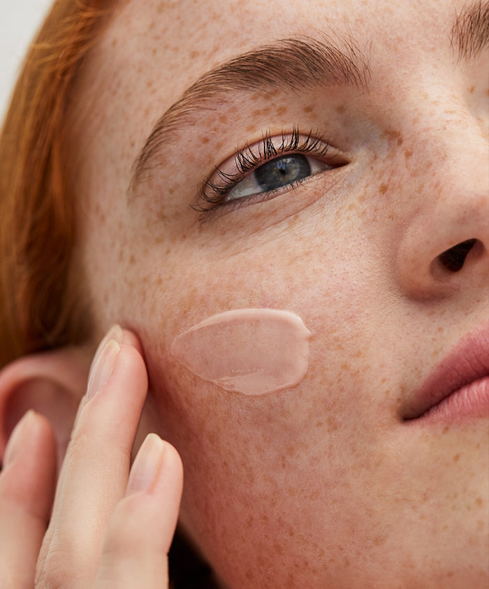 Close-up of a woman with freckles applying a smooth, light primer cream to her cheek using her fingers, showcasing skincare application for The Prep & Set Duo.