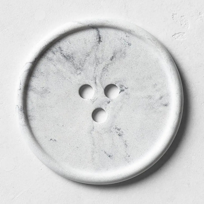 The UME - GREY MARBLE BOUTON ERODE SOAP DISH by UME STUDIO, featuring three holes in a triangle pattern, rests on a smooth matching gray surface.