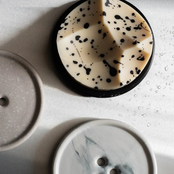 The UME - GREY MARBLE BOUTON ERODE SOAP DISH by UME STUDIO, featuring three holes in a triangle pattern, rests on a smooth matching gray surface.