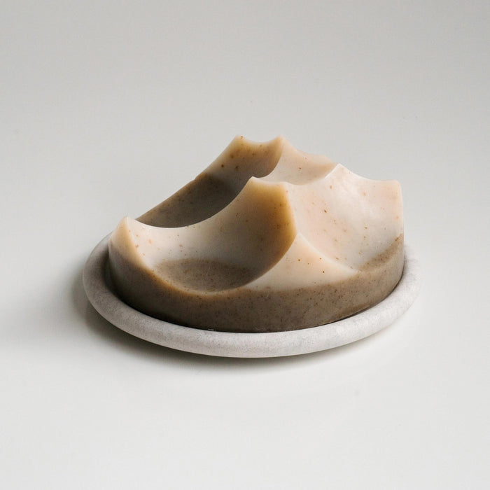 The UME - GREY MARBLE BOUTON ERODE SOAP DISH by UME STUDIO, featuring three holes in a triangle pattern, rests on a smooth matching gray surface.