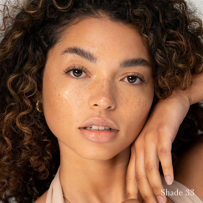 Close-up portrait of a woman with natural makeup featuring RMS Beauty's UnCoverup Concealer in shade 33, highlighting her clear skin and subtle freckles.