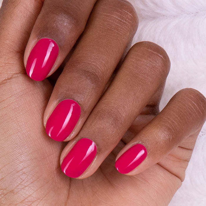 A hand with medium-brown skin shows four fingers with short, glossy pink-green nails painted using the Manucurist You  Me at a Tea Party Green Set. The background is soft and white.