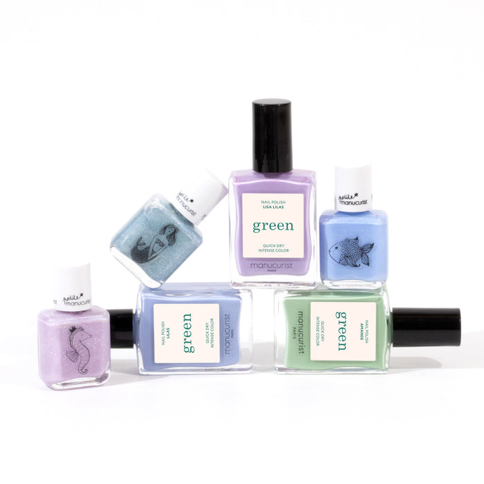 Six bottles of Manucurist’s You  Me Under the Sea Green Set water-based nail polish in pastel aquatic shades (lavender, blue, mint green, purple) are arranged on white. Some green bottles feature sea animal illustrations on the labels.